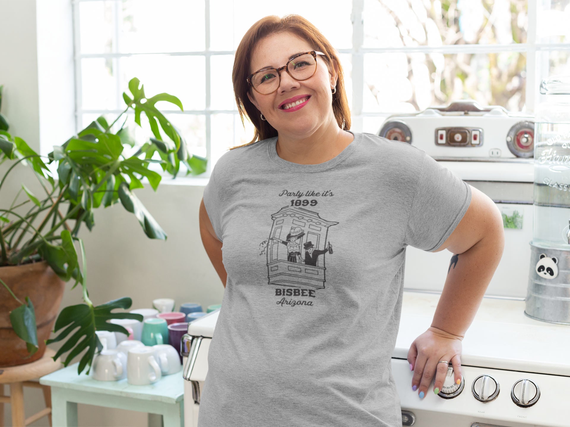 Woman wearing a gray t-shirt that depicts a couple celebrating in early Bisbee, Arizona