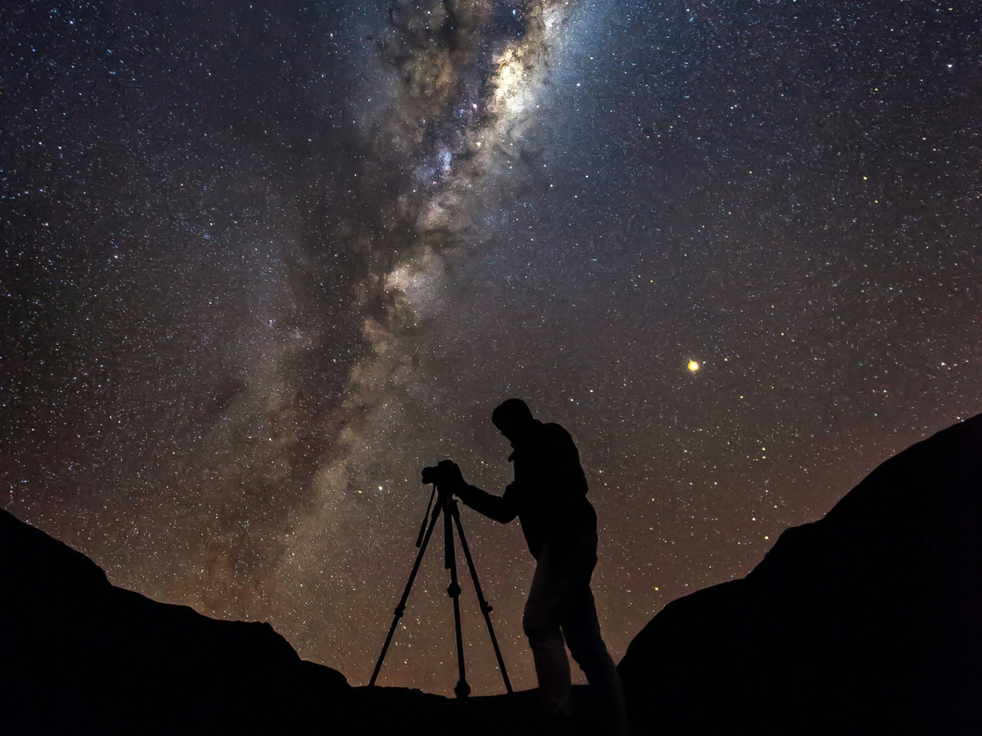 Person with camera equipment under a starry sky with the Milky Way galaxy.